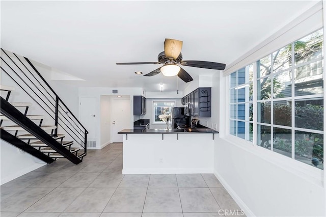 kitchen with kitchen peninsula, black refrigerator, ceiling fan, blue cabinetry, and light tile patterned flooring