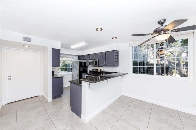 kitchen featuring light tile patterned floors, kitchen peninsula, ceiling fan, stainless steel appliances, and a breakfast bar