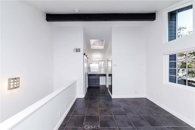 hallway featuring a skylight, dark tile patterned flooring, and beamed ceiling