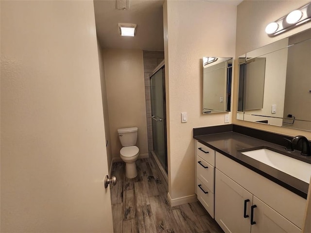 bathroom with hardwood / wood-style floors, toilet, a shower with shower door, and vanity