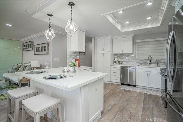 kitchen with white cabinetry, stainless steel appliances, sink, ornamental molding, and a raised ceiling