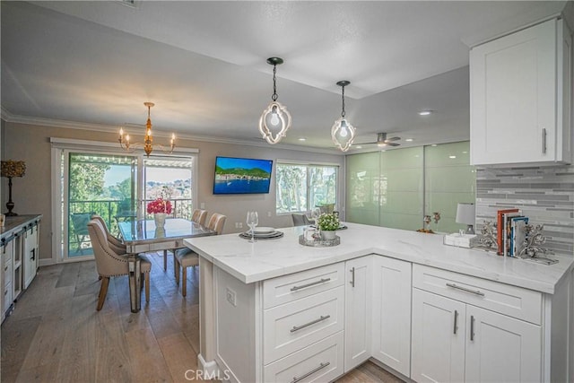 kitchen with tasteful backsplash, kitchen peninsula, light stone counters, and white cabinetry