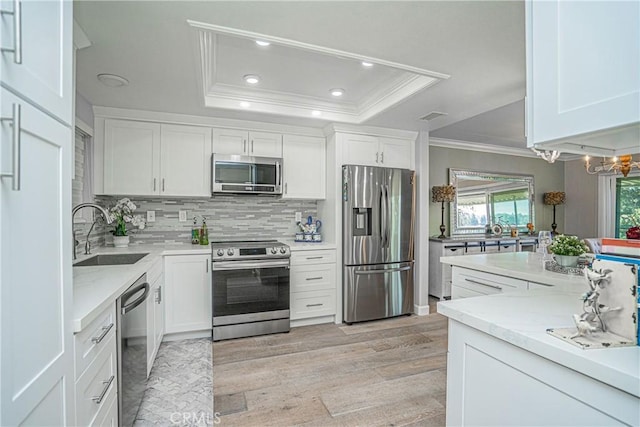 kitchen with white cabinets, appliances with stainless steel finishes, sink, and a tray ceiling