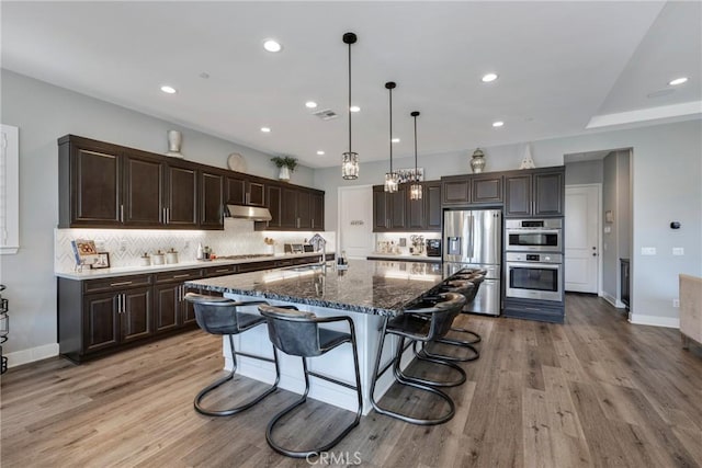 kitchen featuring stainless steel appliances, a kitchen breakfast bar, pendant lighting, a kitchen island with sink, and light wood-type flooring