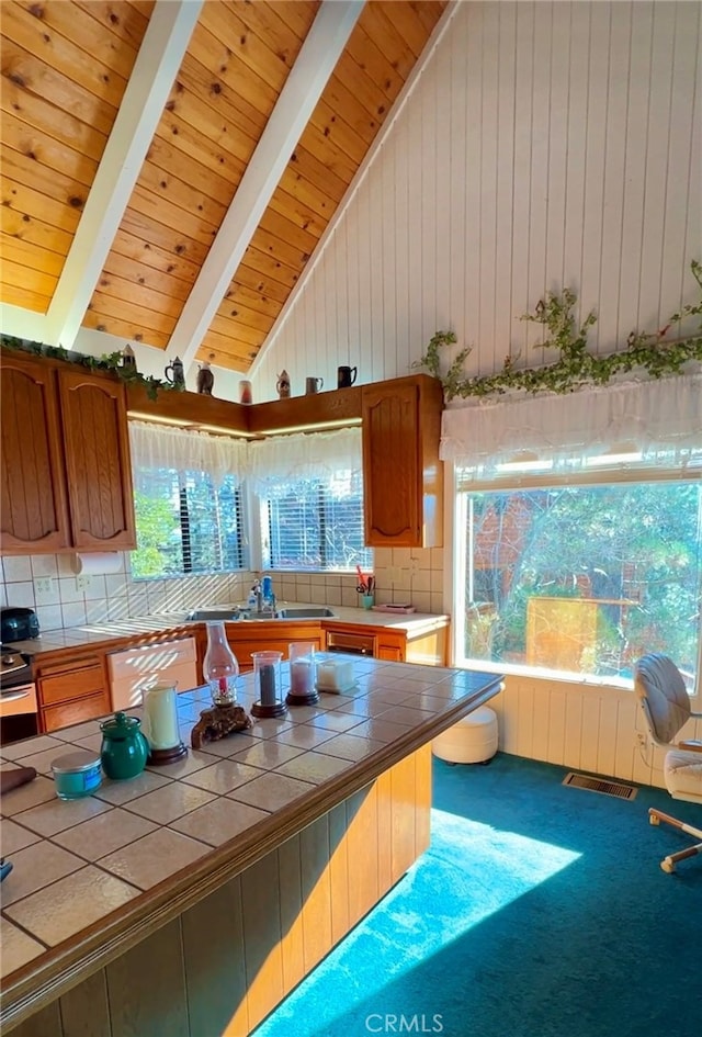 kitchen with plenty of natural light, beamed ceiling, tile countertops, and carpet flooring