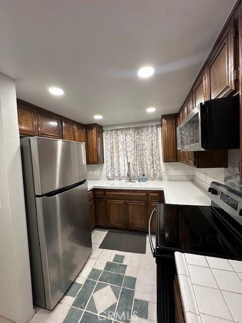 kitchen featuring dark brown cabinetry, stainless steel appliances, tile counters, and sink