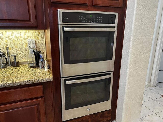 kitchen featuring tasteful backsplash, light tile patterned floors, double oven, and light stone counters