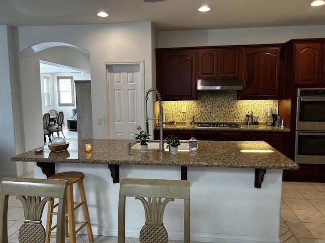 kitchen featuring sink, appliances with stainless steel finishes, dark stone countertops, and a breakfast bar area