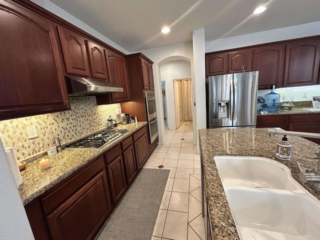 kitchen featuring backsplash, sink, stainless steel appliances, light tile patterned floors, and stone countertops