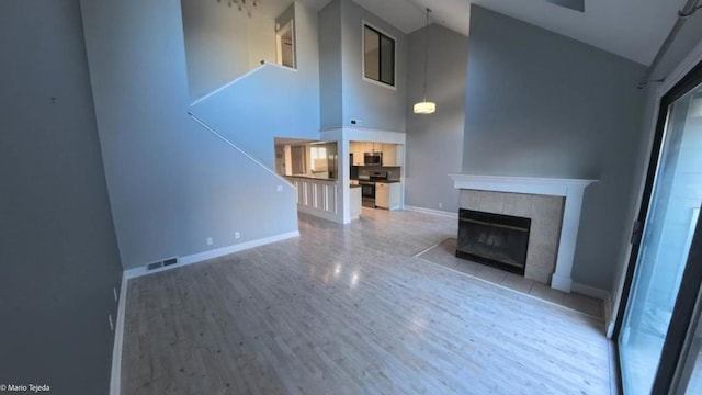 unfurnished living room featuring wood-type flooring, high vaulted ceiling, and a tiled fireplace