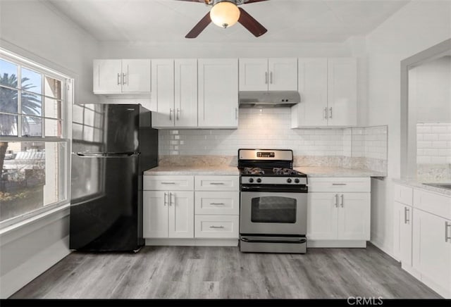 kitchen featuring gas stove, white cabinetry, black fridge, backsplash, and light wood-type flooring