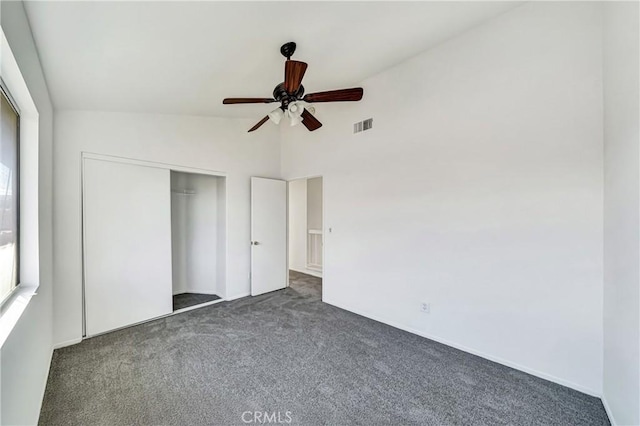 unfurnished bedroom featuring lofted ceiling, a closet, visible vents, dark colored carpet, and a ceiling fan