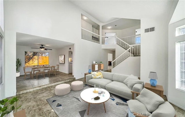 living room with ceiling fan, a high ceiling, visible vents, baseboards, and stairs