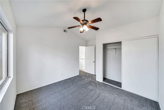 unfurnished bedroom featuring lofted ceiling, a closet, visible vents, dark carpet, and ceiling fan