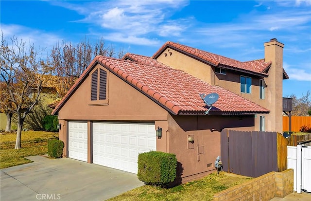 view of side of home featuring concrete driveway, a chimney, a tiled roof, fence, and stucco siding