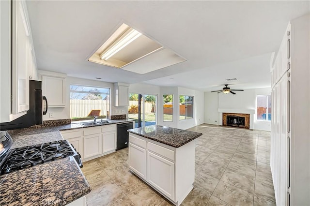 kitchen featuring black dishwasher, a kitchen island, a fireplace, white cabinetry, and a sink