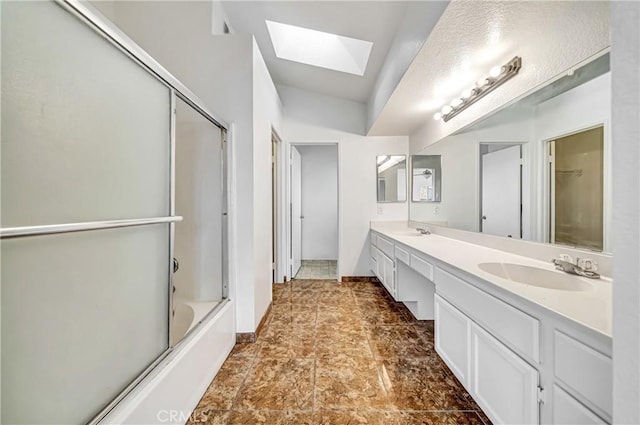 bathroom featuring a skylight, combined bath / shower with glass door, a sink, and double vanity