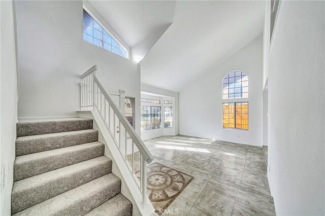 stairs with high vaulted ceiling and a healthy amount of sunlight