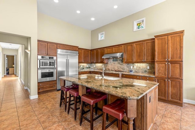 kitchen with a towering ceiling, stainless steel appliances, sink, a kitchen island with sink, and a breakfast bar area