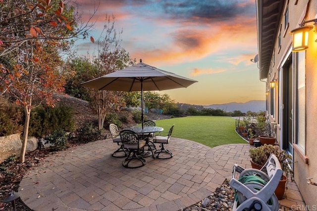 patio terrace at dusk featuring a mountain view and a lawn