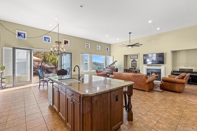 kitchen featuring a center island with sink, sink, light tile patterned flooring, light stone countertops, and ceiling fan with notable chandelier