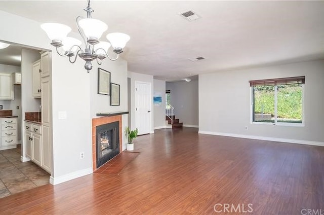 unfurnished living room featuring a chandelier, a fireplace with flush hearth, wood finished floors, baseboards, and visible vents