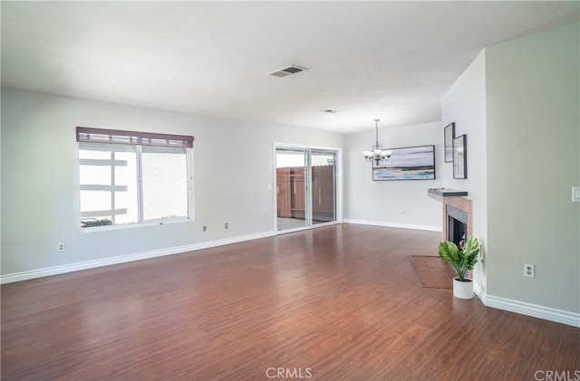 unfurnished living room with visible vents, baseboards, a fireplace with flush hearth, dark wood-type flooring, and a notable chandelier