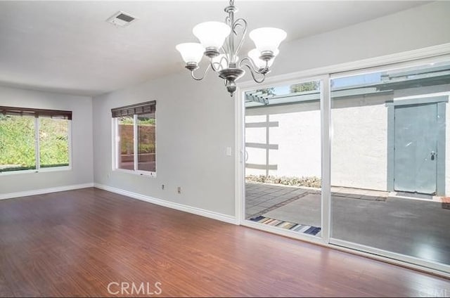 unfurnished dining area with baseboards, visible vents, a chandelier, and wood finished floors