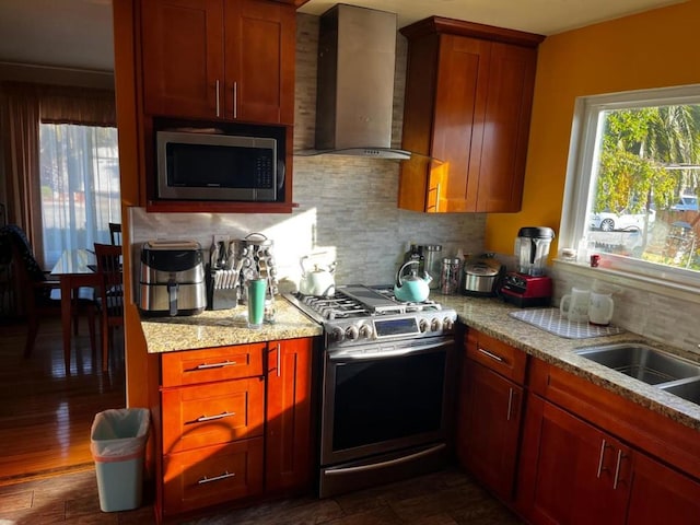 kitchen with stainless steel appliances, light stone countertops, wall chimney exhaust hood, sink, and backsplash