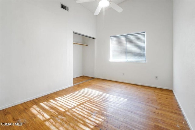 unfurnished bedroom featuring ceiling fan, wood-type flooring, a towering ceiling, and a closet