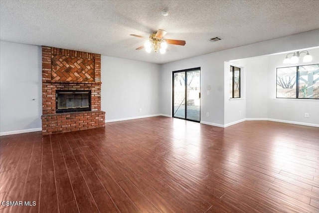 unfurnished living room featuring a textured ceiling, ceiling fan, dark wood-type flooring, and a brick fireplace