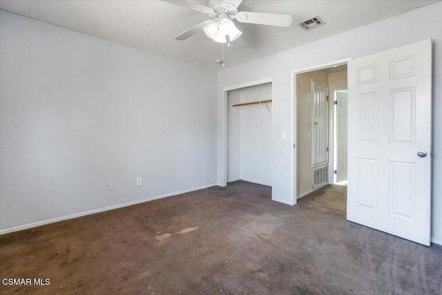 unfurnished bedroom with a textured ceiling, dark carpet, a closet, and ceiling fan