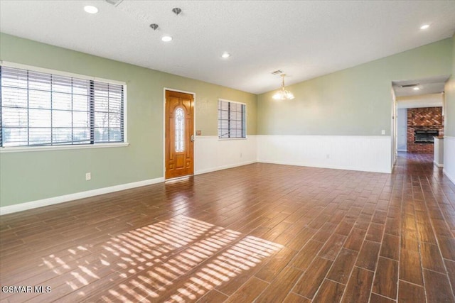 spare room featuring a notable chandelier, a fireplace, dark wood-type flooring, and vaulted ceiling