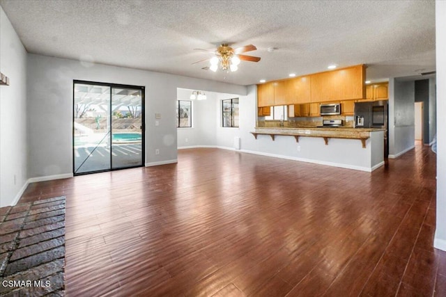 unfurnished living room featuring ceiling fan, dark wood-type flooring, and a textured ceiling