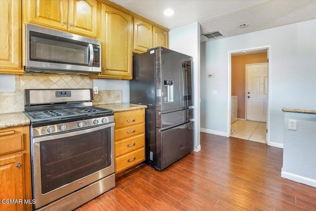 kitchen featuring light stone countertops, appliances with stainless steel finishes, dark hardwood / wood-style flooring, and tasteful backsplash