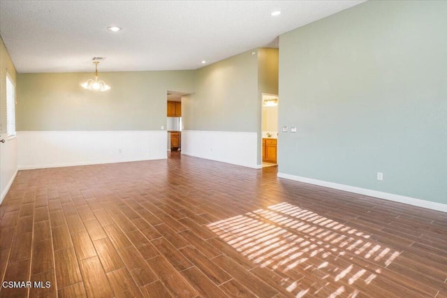 unfurnished room with a textured ceiling, dark hardwood / wood-style flooring, vaulted ceiling, and an inviting chandelier