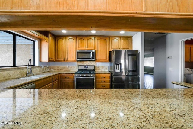 kitchen featuring light stone countertops, sink, tasteful backsplash, washing machine and dryer, and appliances with stainless steel finishes