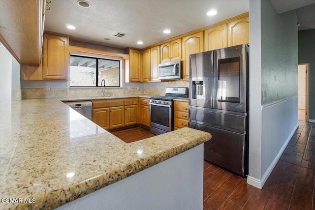 kitchen with kitchen peninsula, appliances with stainless steel finishes, dark hardwood / wood-style flooring, and light stone counters