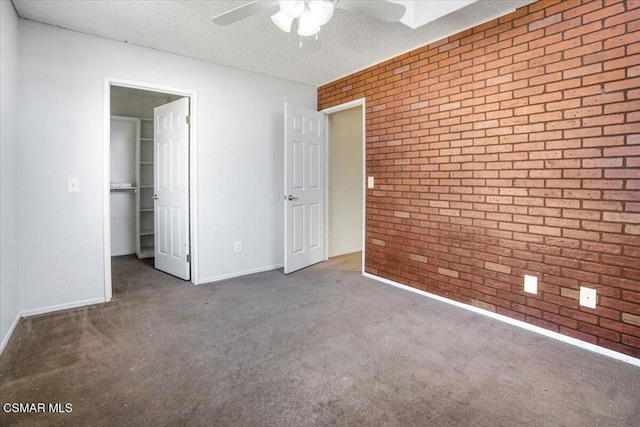 unfurnished room with ceiling fan, brick wall, a textured ceiling, and dark carpet