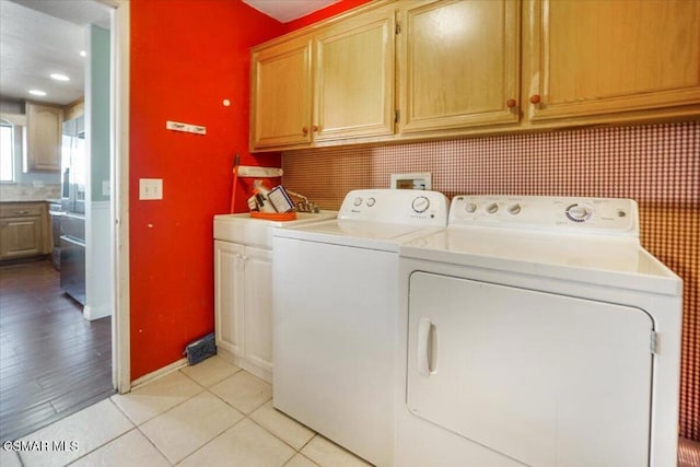 clothes washing area featuring washer and clothes dryer, light tile patterned flooring, and cabinets