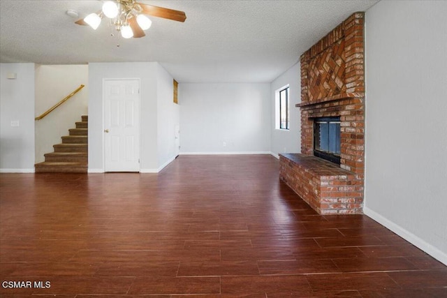 unfurnished living room featuring ceiling fan, dark hardwood / wood-style flooring, a textured ceiling, and a brick fireplace