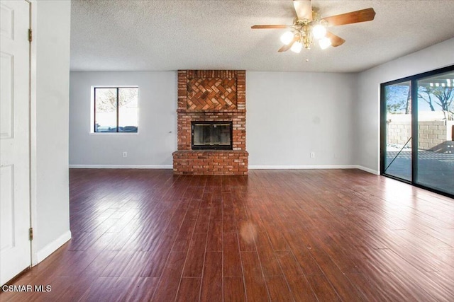 unfurnished living room featuring ceiling fan, a fireplace, dark wood-type flooring, and a textured ceiling