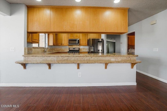 kitchen with kitchen peninsula, a breakfast bar, dark hardwood / wood-style floors, and appliances with stainless steel finishes