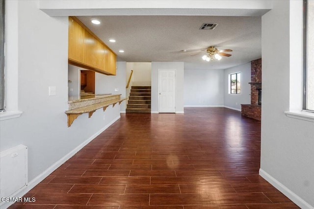 unfurnished living room featuring a fireplace, a textured ceiling, dark hardwood / wood-style flooring, and ceiling fan