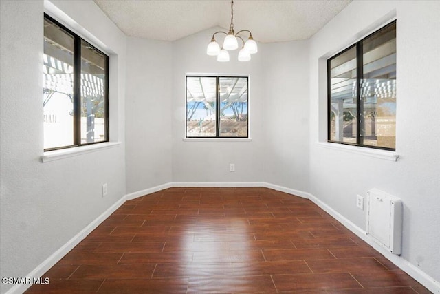 spare room featuring a notable chandelier, plenty of natural light, dark hardwood / wood-style floors, and a textured ceiling