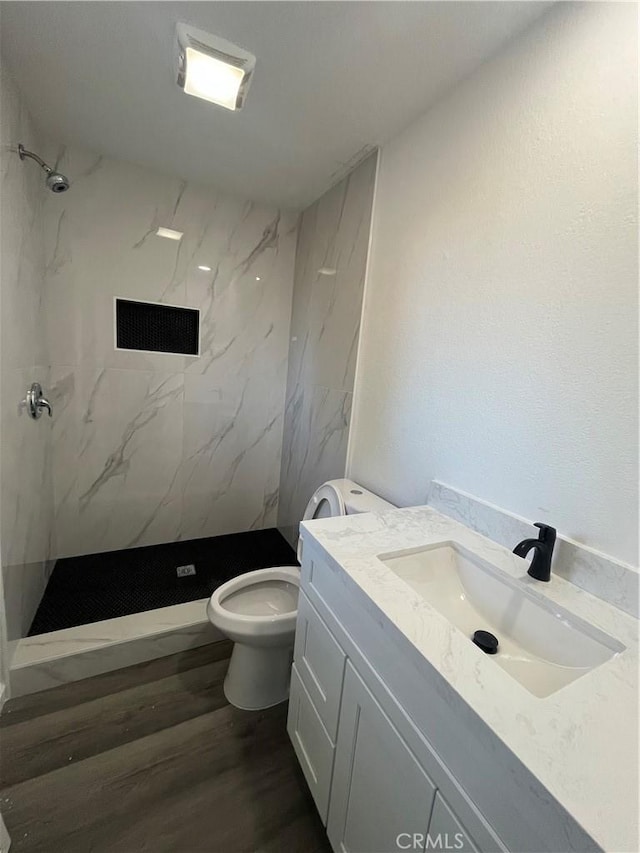 bathroom with tiled shower, wood-type flooring, vanity, and toilet