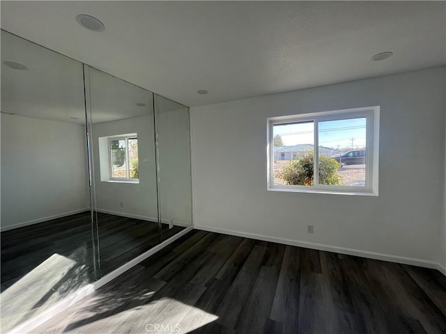 unfurnished bedroom featuring dark hardwood / wood-style floors, a closet, and multiple windows