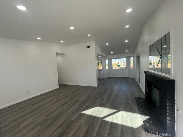 unfurnished living room with lofted ceiling, a brick fireplace, and dark wood-type flooring