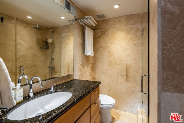 bathroom with an enclosed shower, vanity, toilet, and tile walls