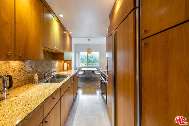 kitchen with pendant lighting, backsplash, sink, light stone countertops, and stainless steel range oven